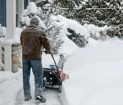 Residential snow removal technician using a snow blower to clear a home driveway and walkway in Dover, DE